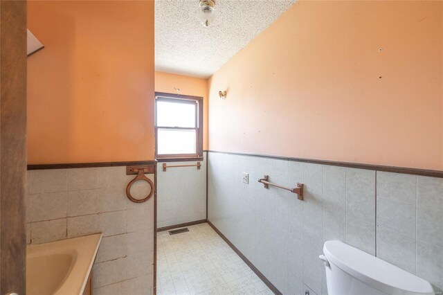 104 E Jefferson Ave, Richland, MO 65556 - bathroom featuring tile walls, a wainscoted wall, a textured ceiling, toilet, and tile patterned floors