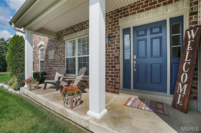 entrance to property featuring a porch and brick siding