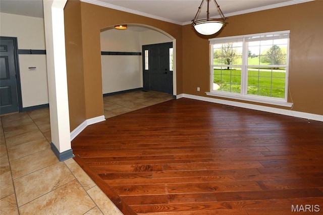 unfurnished dining area featuring wood-type flooring, crown molding, arched walkways, and baseboards