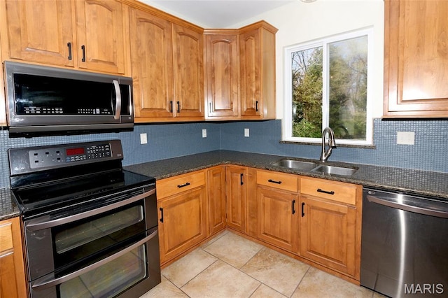 kitchen featuring stainless steel appliances, a sink, dark stone countertops, and light tile patterned floors