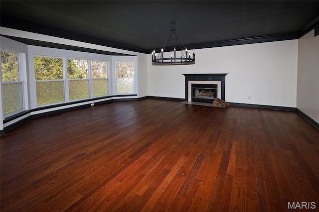 unfurnished living room featuring a chandelier, baseboards, plenty of natural light, and dark wood-type flooring