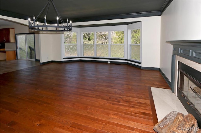unfurnished dining area featuring a fireplace with flush hearth, a chandelier, wood finished floors, baseboards, and ornamental molding