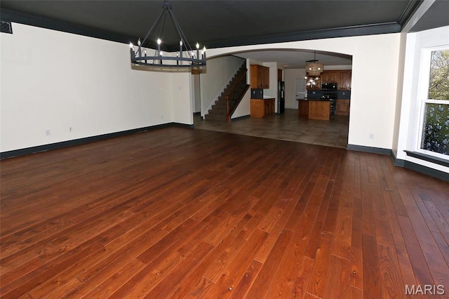 unfurnished dining area featuring a chandelier, arched walkways, dark wood finished floors, baseboards, and ornamental molding