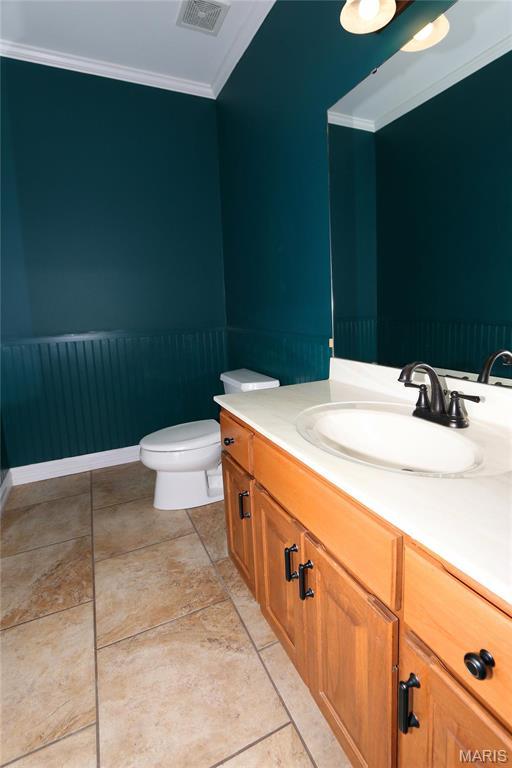 half bath featuring ornamental molding, vanity, and toilet