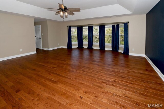 spare room with a raised ceiling, a ceiling fan, wood finished floors, and baseboards