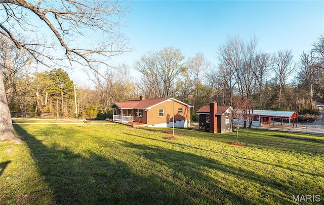 view of green lawn with covered porch, a detached carport, and an outbuilding