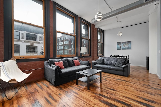 living room featuring wood-type flooring, brick wall, and baseboards