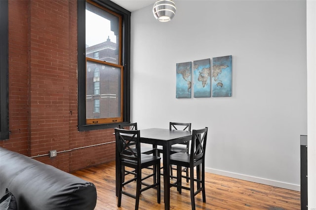 dining room featuring wood finished floors, brick wall, and baseboards
