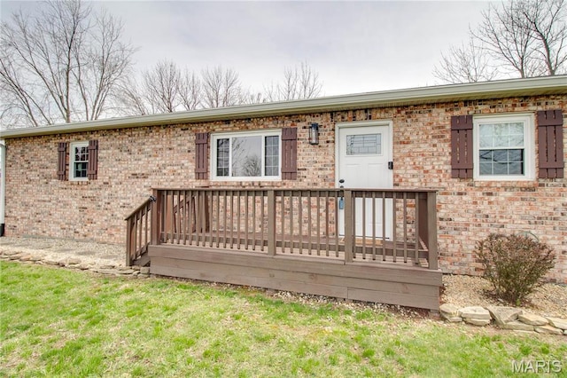back of house with brick siding, a deck, and a yard