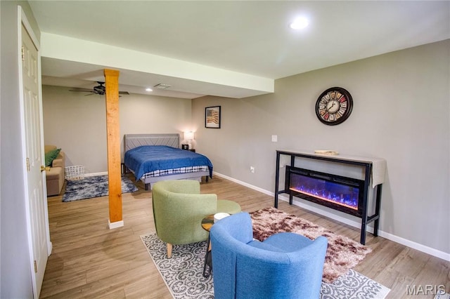bedroom with baseboards, wood finished floors, a glass covered fireplace, and recessed lighting