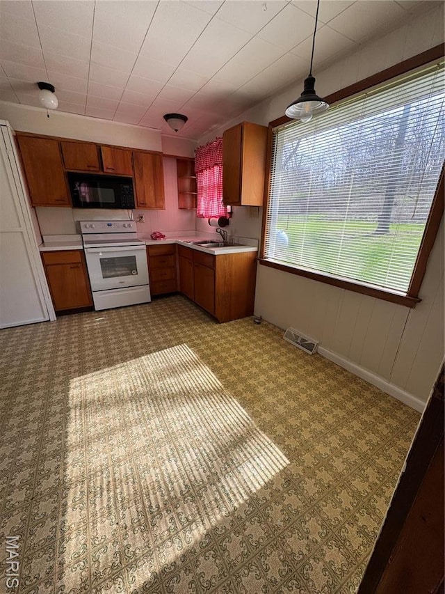 13899 Riverview Dr, New London, MO 63459 - kitchen with white range with electric stovetop, black microwave, brown cabinets, light countertops, and a sink