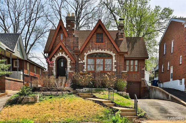 7414 Bruno Ave, Saint Louis, MO 63117 - tudor-style house with brick siding, a chimney, driveway, a garage, and roof with shingles