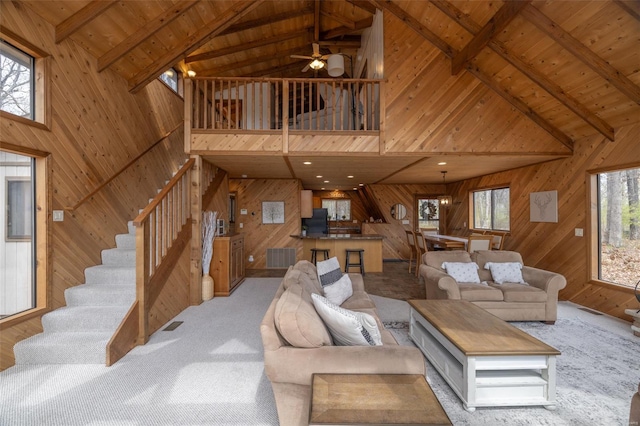 carpeted living room featuring high vaulted ceiling, wooden walls, stairway, wood ceiling, and ceiling fan