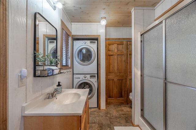 bathroom with stacked washing machine and dryer, a stall shower, vanity, wooden ceiling, and toilet