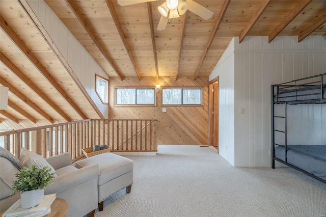 living area featuring wooden walls, beam ceiling, carpet floors, a ceiling fan, and an upstairs landing