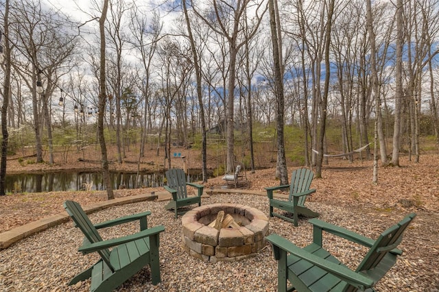 view of home's community with an outdoor fire pit and view of wooded area