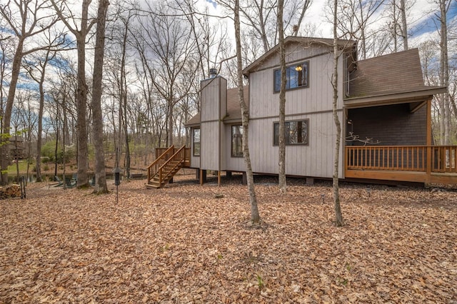 back of house with roof with shingles, a deck, a chimney, and stairway