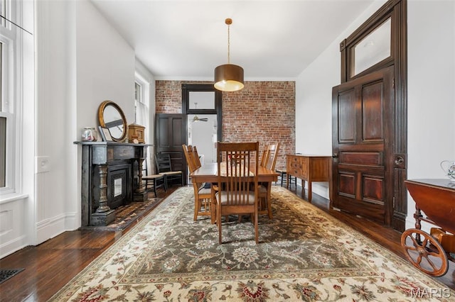dining room with dark wood-type flooring, brick wall, a fireplace with flush hearth, and baseboards