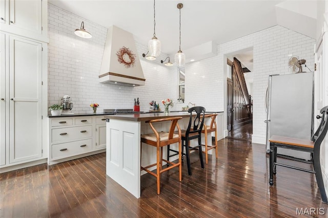 kitchen featuring dark countertops, custom exhaust hood, a kitchen breakfast bar, freestanding refrigerator, and dark wood-type flooring