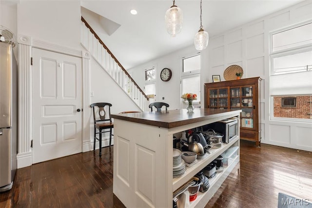 kitchen featuring dark wood-style flooring, a decorative wall, appliances with stainless steel finishes, white cabinetry, and hanging light fixtures