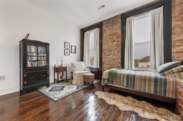 bedroom with wood finished floors, brick wall, and baseboards