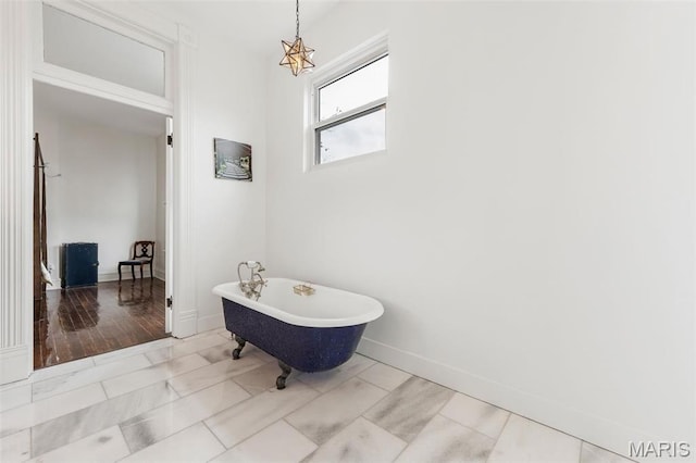 bathroom with marble look tiles, a freestanding bath, and baseboards