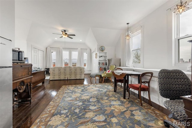 living area with a ceiling fan, healthy amount of natural light, vaulted ceiling, dark wood finished floors, and baseboards