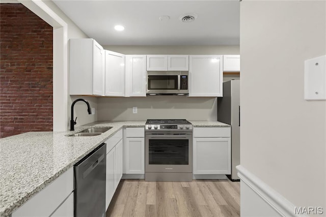 914 Russell Blvd, Saint Louis, MO 63104 - kitchen with stainless steel appliances, brick wall, light wood-style floors, and white cabinetry