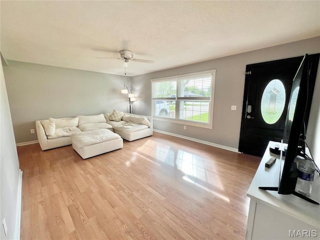 living area with light wood-style floors, a ceiling fan, baseboards, and a textured ceiling