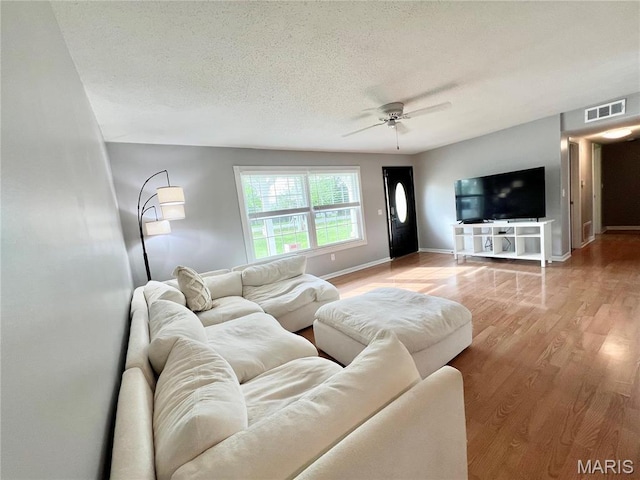 living area featuring a ceiling fan, wood finished floors, a textured ceiling, and baseboards