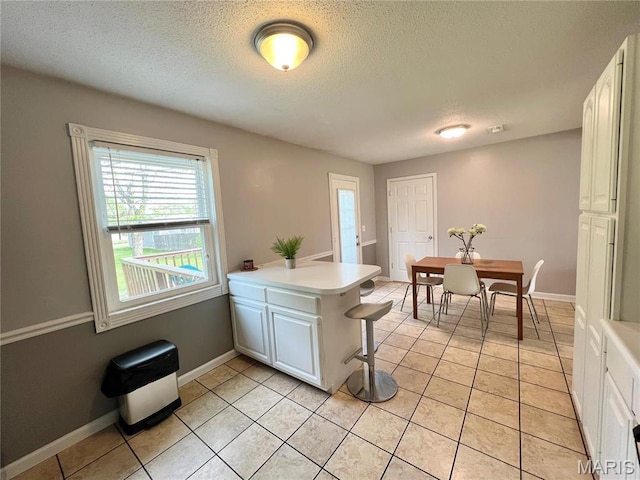 kitchen with a peninsula, white cabinetry, light countertops, baseboards, and a textured ceiling