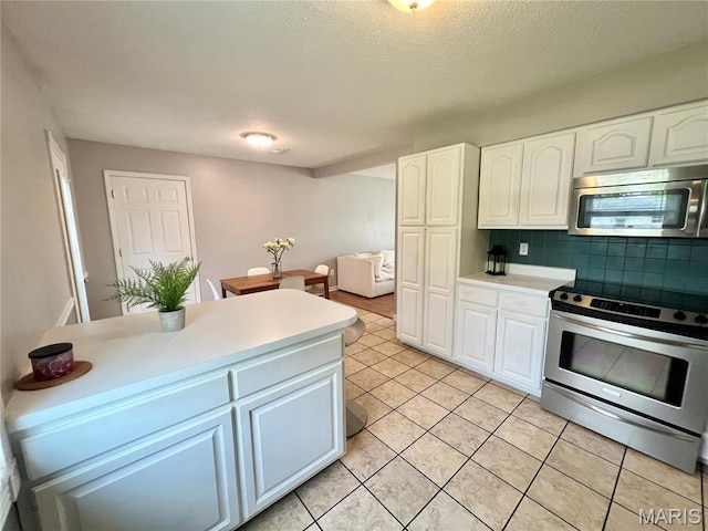 kitchen with appliances with stainless steel finishes, tasteful backsplash, white cabinets, light tile patterned floors, and light countertops