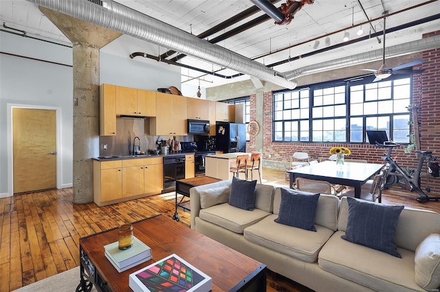 living room with light wood-type flooring, brick wall, a high ceiling, and ceiling fan