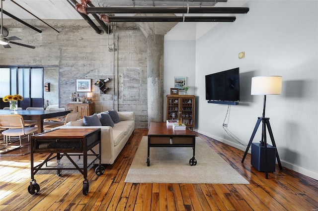 living room with a towering ceiling, hardwood / wood-style floors, a ceiling fan, and baseboards