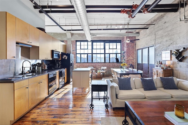 living room featuring wood-type flooring, a towering ceiling, brick wall, and healthy amount of natural light