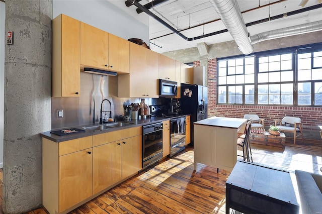 kitchen with black appliances, a sink, hardwood / wood-style flooring, light brown cabinets, and dark countertops