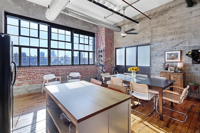 dining space with a towering ceiling, hardwood / wood-style flooring, brick wall, and a ceiling fan