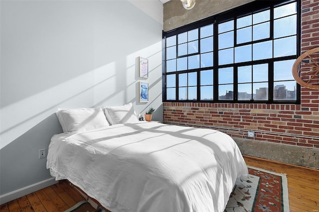 bedroom featuring hardwood / wood-style flooring, baseboards, brick wall, and multiple windows