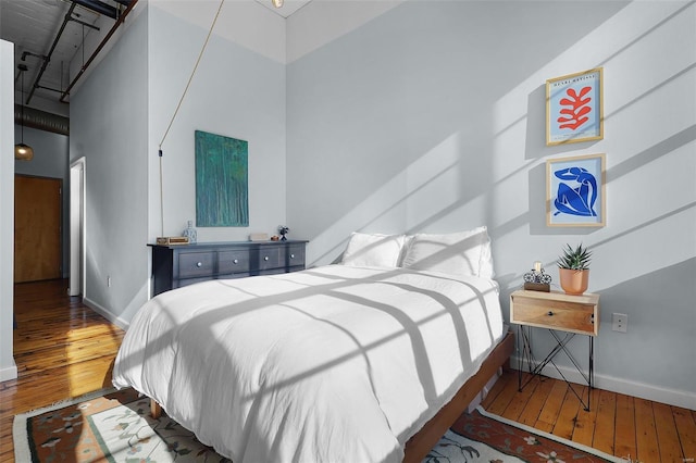 bedroom with wood-type flooring, a high ceiling, and baseboards