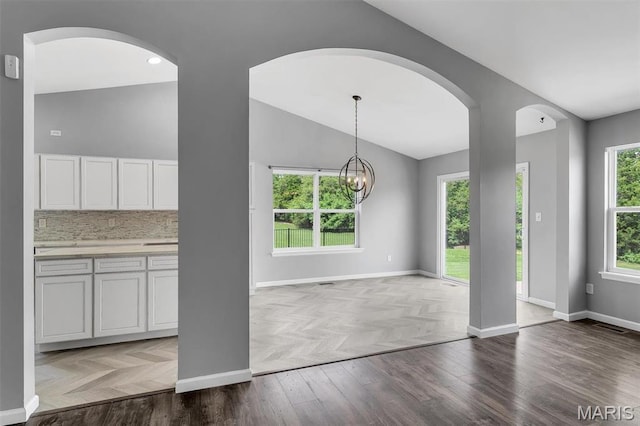 283 Sonnet Cir, Wentzville, MO 63385 - unfurnished dining area featuring vaulted ceiling, baseboards, arched walkways, a chandelier, and parquet floors