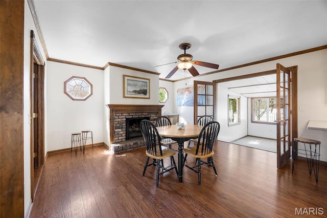 dining space featuring wood finished floors, baseboards, crown molding, ceiling fan, and a fireplace