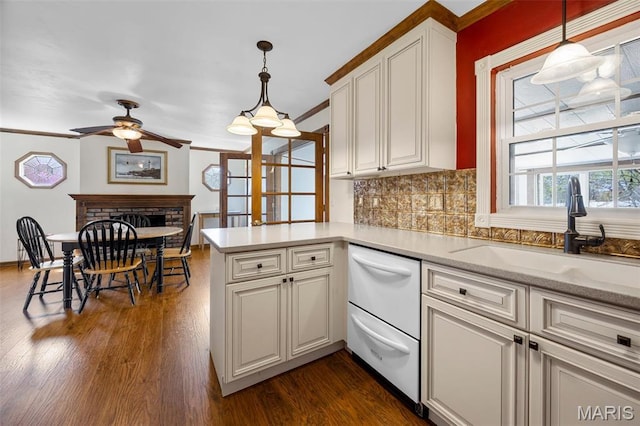 kitchen with a sink, a ceiling fan, a peninsula, dishwasher, and backsplash