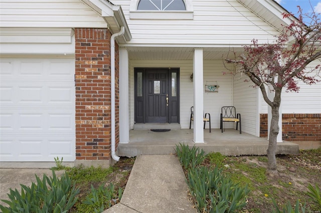 entrance to property featuring a porch, brick siding, and a garage