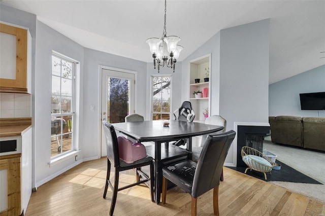dining room with a chandelier, vaulted ceiling, light wood finished floors, and baseboards