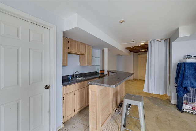 kitchen with light brown cabinets, dark countertops, a sink, a breakfast bar area, and a center island