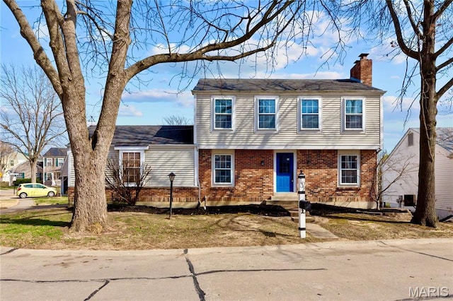 colonial inspired home featuring a chimney, brick siding, and entry steps