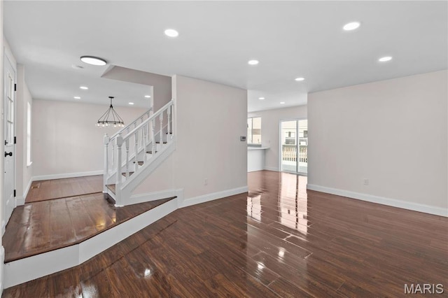 unfurnished living room with stairs, wood finished floors, recessed lighting, baseboards, and a chandelier