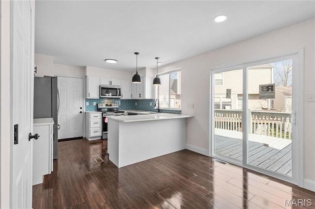 kitchen with stainless steel appliances, a peninsula, light countertops, dark wood-style floors, and baseboards