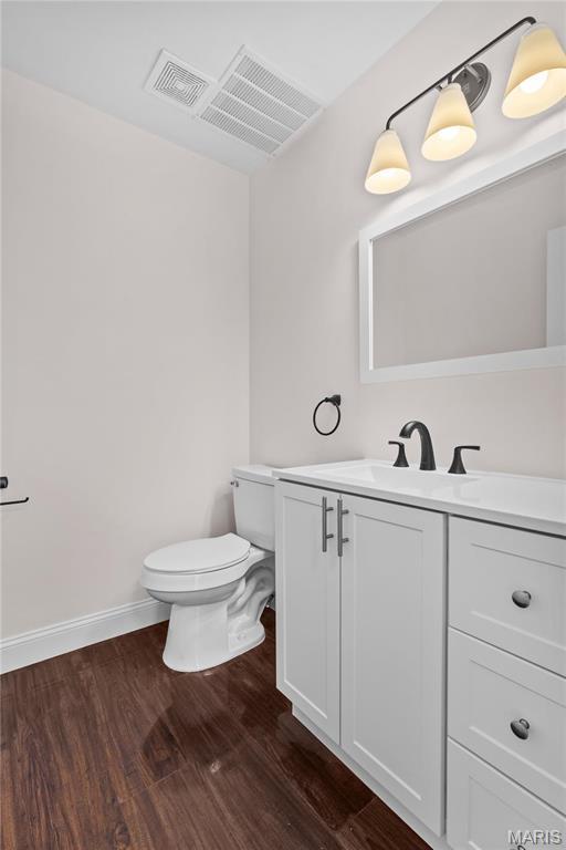 half bath with wood finished floors, toilet, vanity, and baseboards