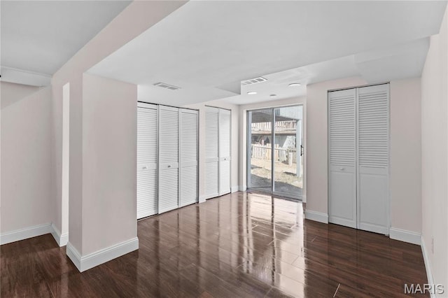 unfurnished bedroom with baseboards, wood finished floors, and two closets